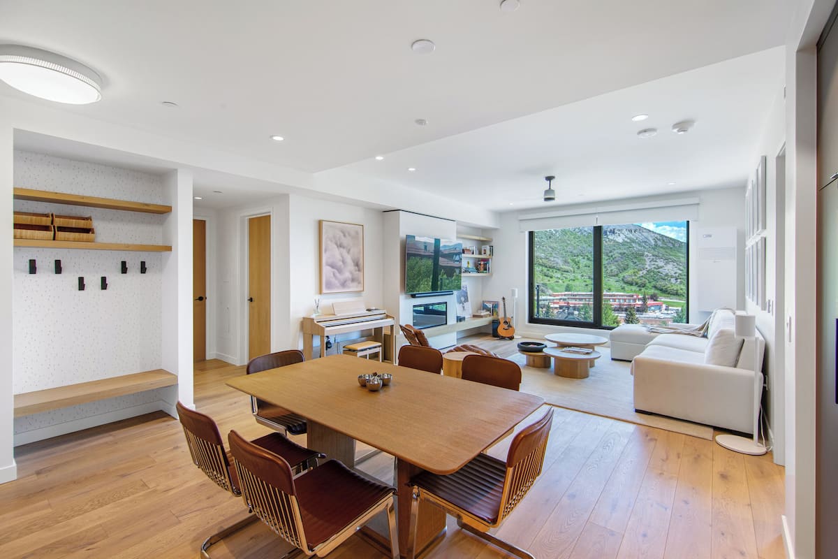 Un espacio habitable amplio con una mesa de comedor de madera, asientos cómodos, un piano y un gran ventanal con vistas a la montaña.