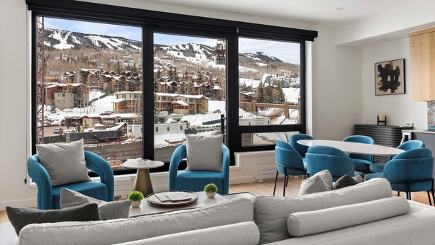 A modern living room with a large window offering a view of a snowy mountain town.