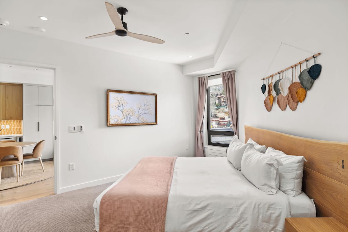 Un dormitorio moderno con cama, ventilador de techo, ventana con cortinas y una planta en la pared.