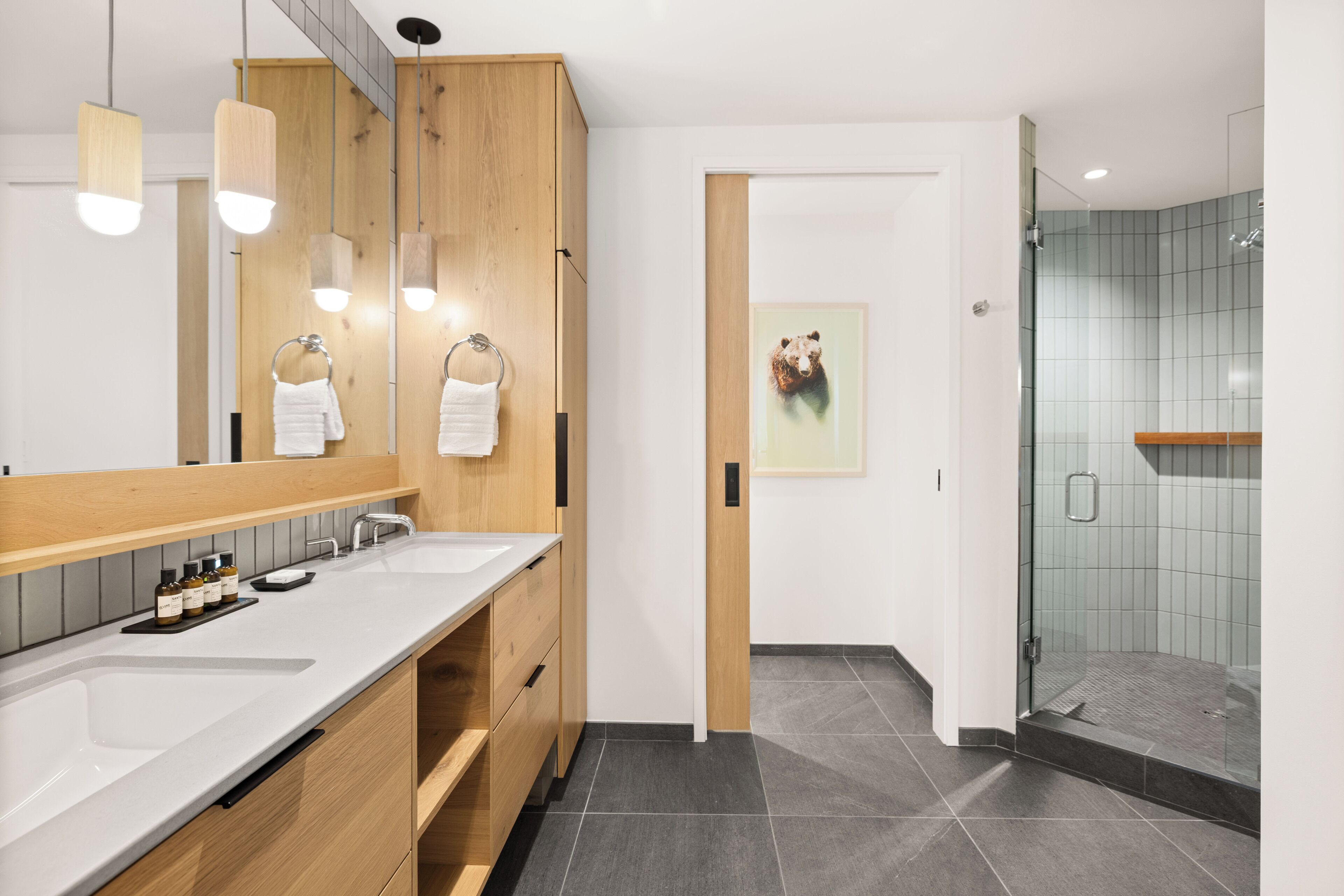 A modern bathroom with a wooden vanity, a large mirror, and a glass shower enclosure.