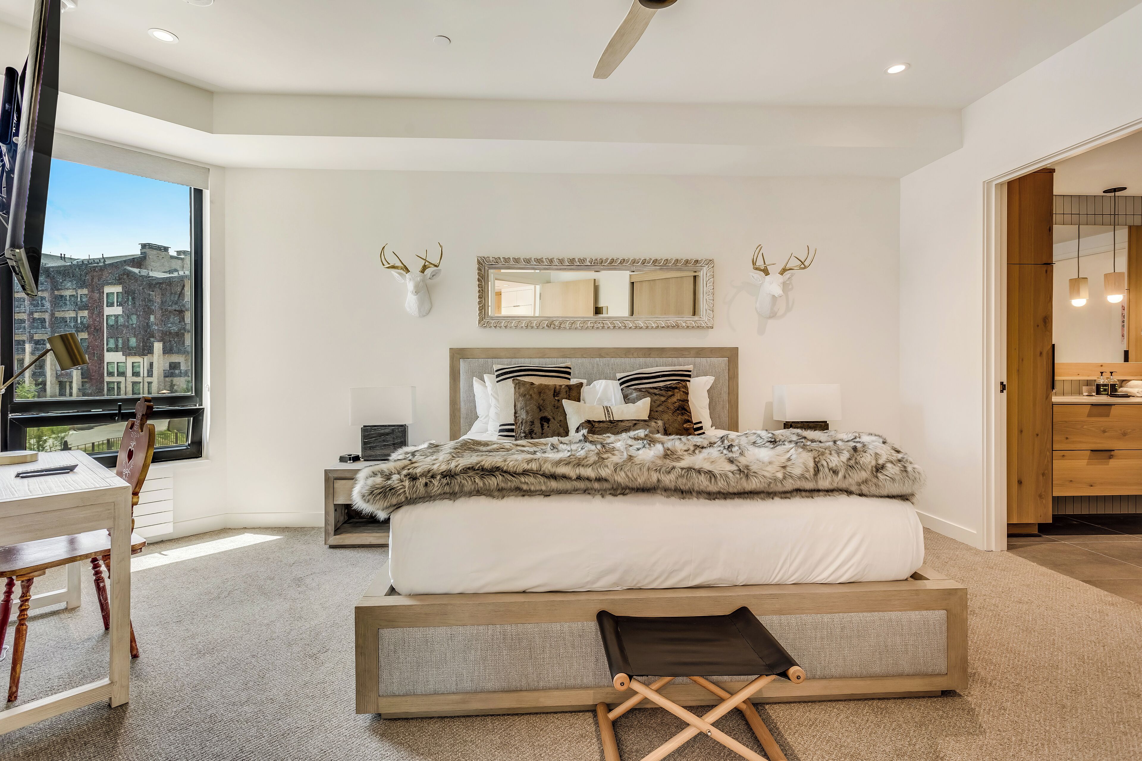 A modern bedroom with a large bed, a desk, and a view of the city.
