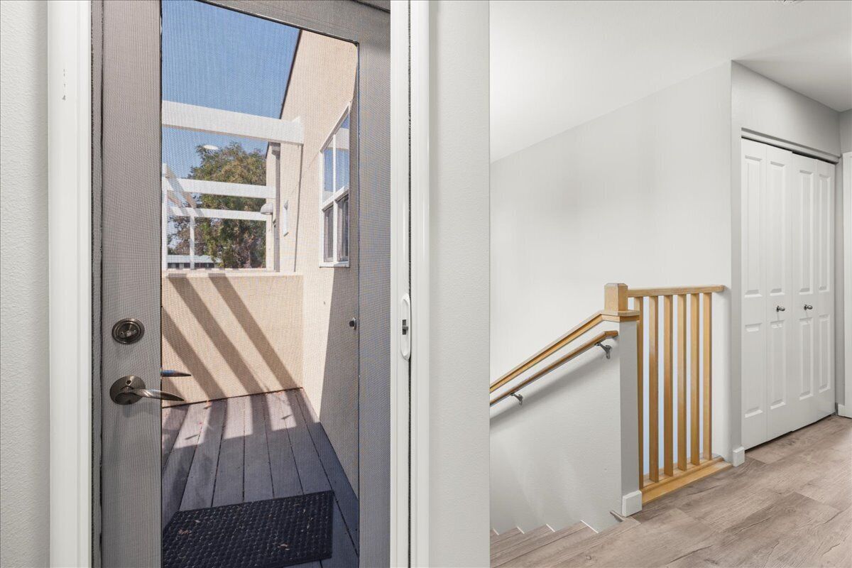 A modern entryway with a door leading to a covered outdoor area, a wooden staircase, and a white door.