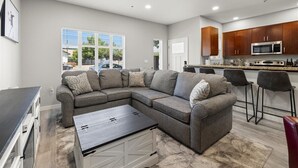 Ein modernes Wohnzimmer mit einem Ecksofa, einem Couchtisch und einer Küchenzeile mit Holzausbau und einer Mikrowelle.