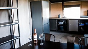 Una cocina moderna con refrigerador empotrado, una mesa de comedor con sillas, y una botella de vino y una copa sobre la mesa.