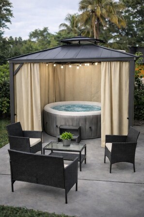 Un bain à remous surmonté d’une pergola, entouré de meubles en osier et d’une table en verre.