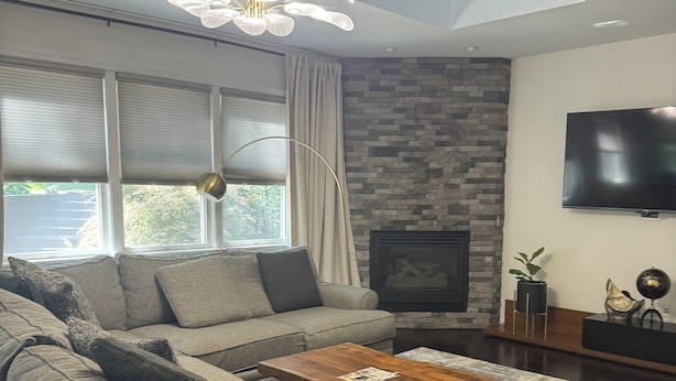 A modern living room with a sectional sofa, a wooden coffee table, a fireplace, a flat-screen TV, and a ceiling fan.