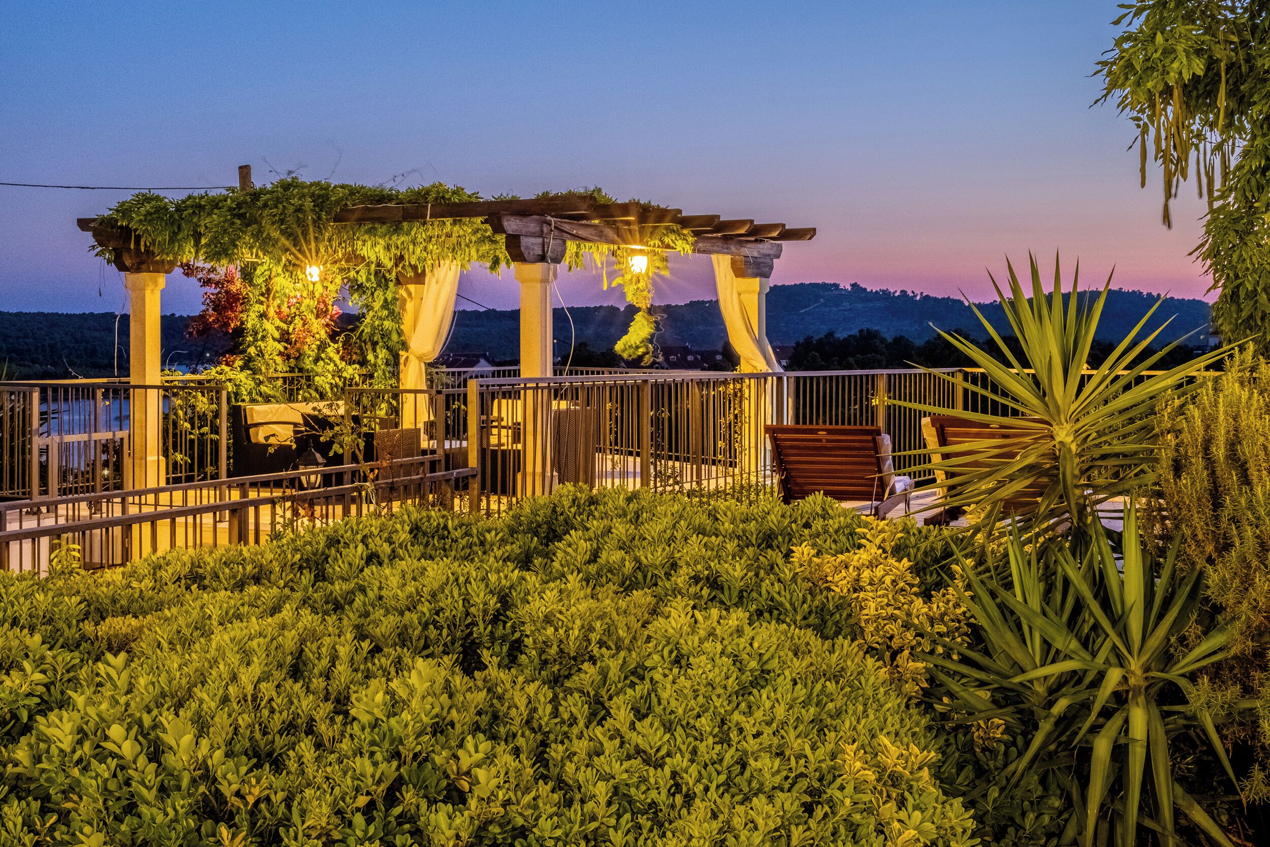 A garden area with a pergola, seating, and a view of the landscape.