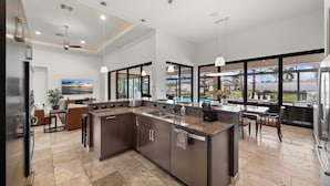 Une cuisine moderne dotée d’un grand îlot central, d’appareils électroménagers en acier inoxydable et offrant une vue sur une piscine et un espace extérieur.