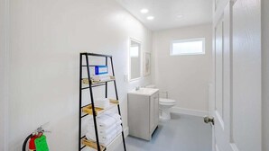 A bathroom with a white sink, toilet, and a shelf with towels. - Hopkins (Biloxi)
