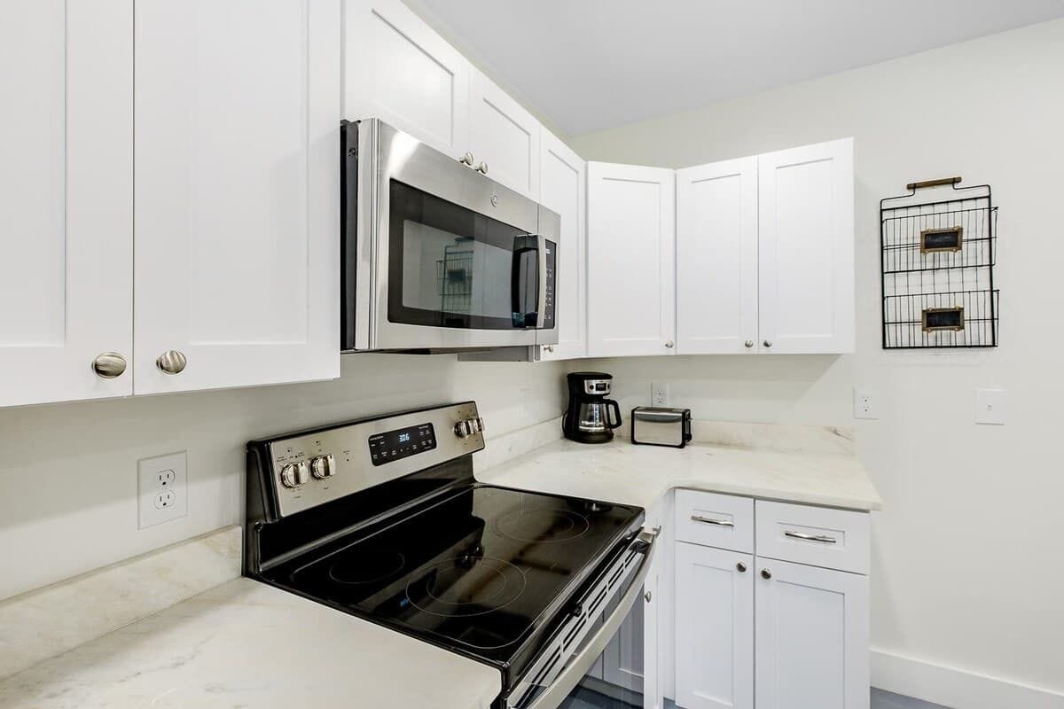 A kitchen with white cabinets, a stainless steel microwave, a black stove, and a coffee maker.