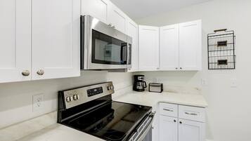 A kitchen with white cabinets, a stainless steel microwave, a black stove, and a coffee maker.