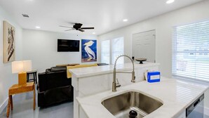 A modern kitchen with a built-in sink, a ceiling fan, and a flat-screen TV mounted on the wall. - Hopkins (Biloxi)