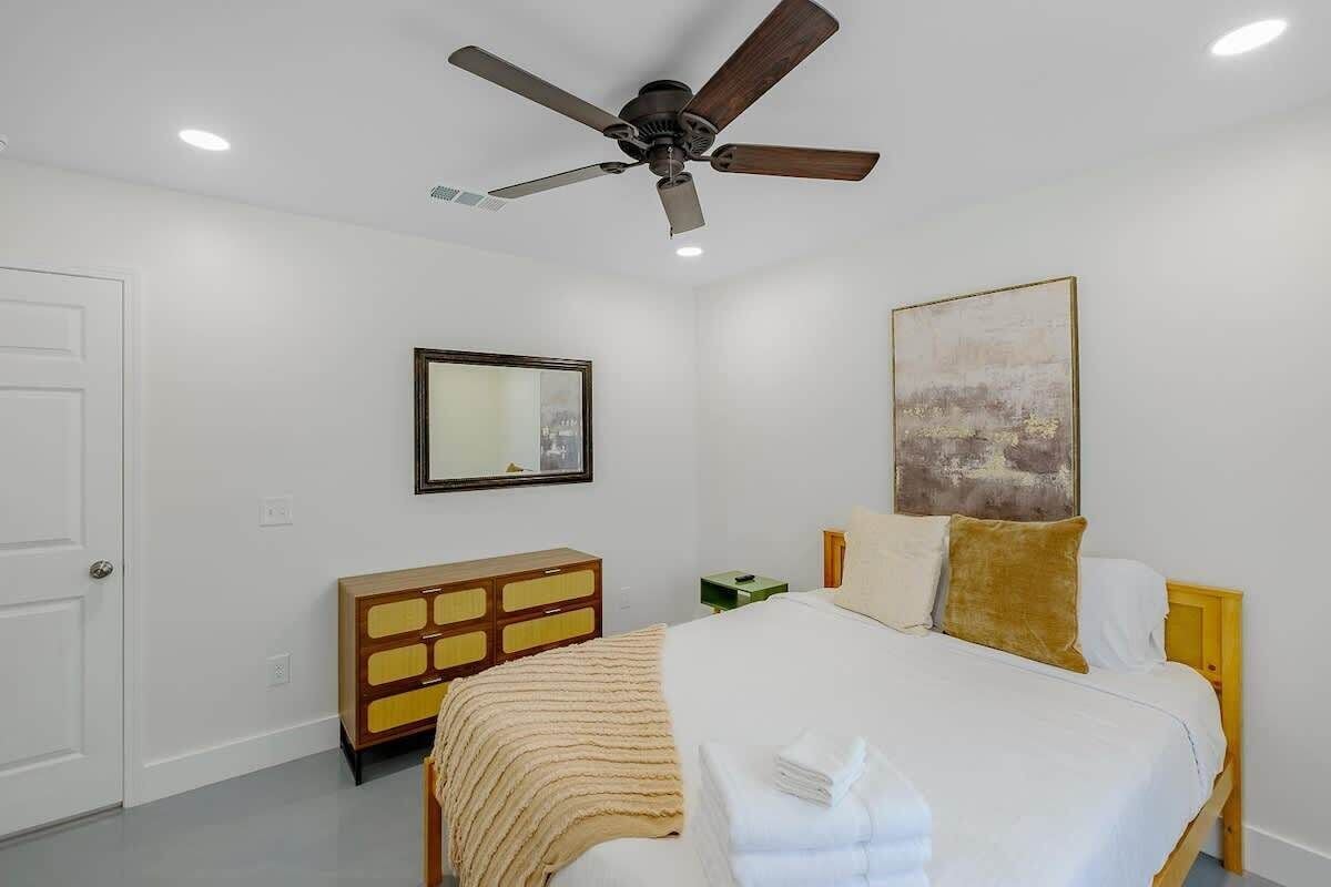 A bedroom with a bed, a ceiling fan, a dresser, a mirror, and a painting on the wall.