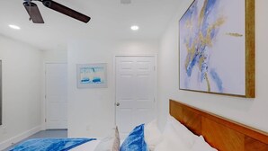 A bedroom with a bed, a ceiling fan, a door, and a painting on the wall. - Hopkins (Biloxi)