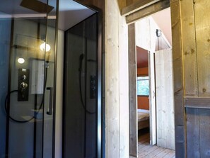 A modern bathroom with a glass shower enclosure, a visible toilet, and a wooden door leading to a bedroom with a bed. - Cozy Tent Lodge With Sanitary Facilities (Enkhuizen)