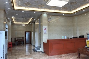 A hotel lobby with a reception desk, a wooden bench, and a tiled floor. - Dongxing Qianghua Business Hotel (Dongxing)