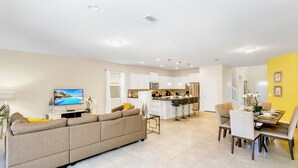 Una sala de estar moderna con un sofá color beige, un televisor de pantalla plana y un comedor con una mesa y sillas.
