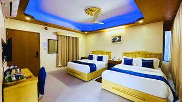 A hotel room with two beds, a desk, a chair, a ceiling fan, and a window with curtains.
