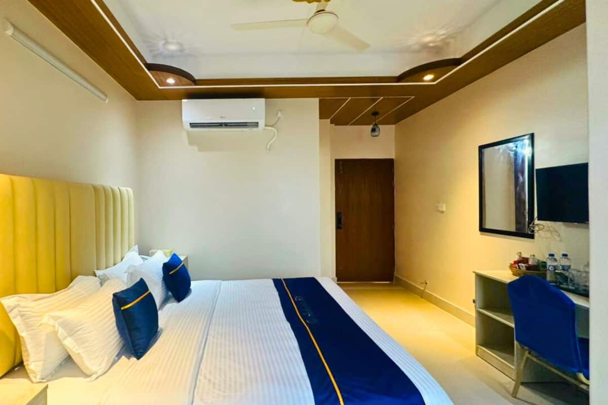 Una habitación de hotel moderna con una cama grande, un ventilador de techo, un equipo de aire acondicionado, techo de madera y un escritorio pequeño con una silla.