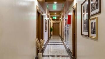 Ein Hotelgang mit Marmorboden, Holzzapfen an der Decke, gerahmten Bildern an den Wänden und einer Zimmerpflanze.