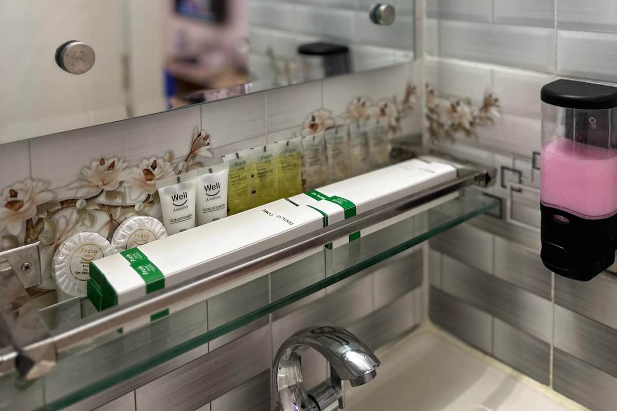 Un baño con un estante de vidrio que contiene artículos de tocador, un espejo y un dispensador de jabón rosa.