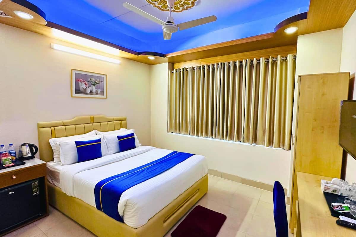 Habitación de hotel con cama, mesita de noche, escritorio, televisor y cortinas.