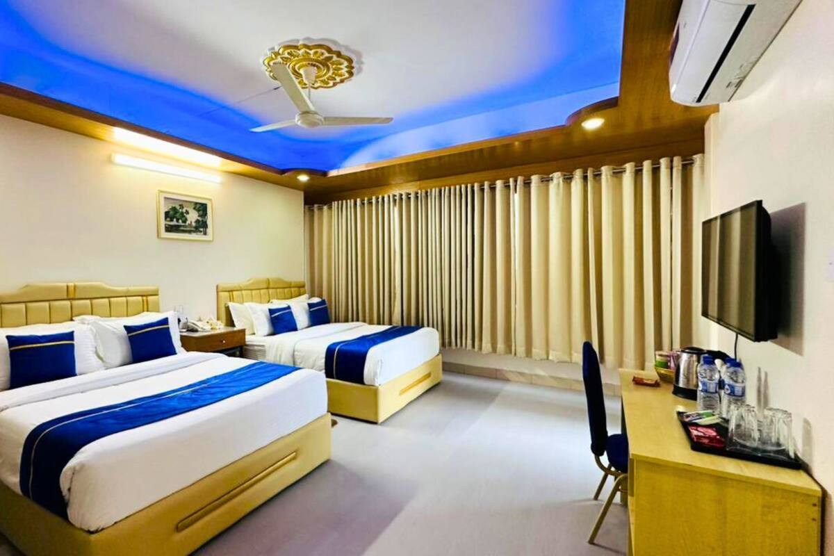 Habitación de hotel con dos camas, ventilador de techo, televisor de pantalla plana y escritorio con silla.