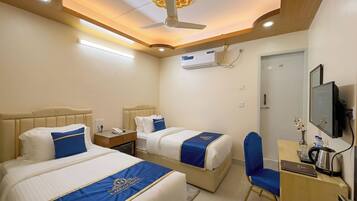 A hotel room with two beds, a desk with a chair, a television, and an air conditioning unit.