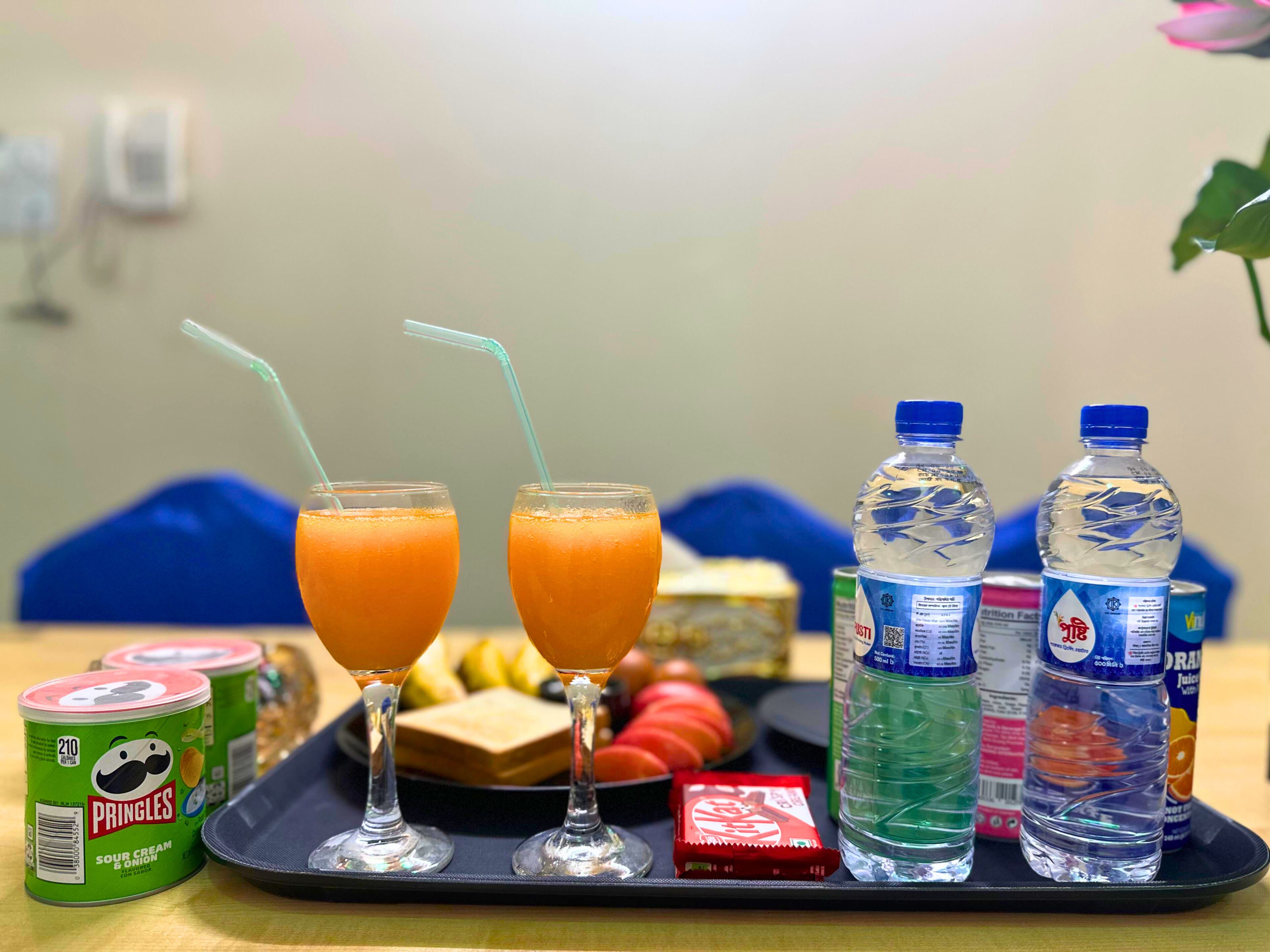 A tray with two glasses of orange juice, two bottles of water, a can of Pringles, and a packet of snacks.