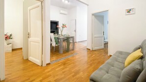 A spacious living area with a wooden floor, a grey sofa with a yellow pillow, and a dining area with a table and chairs. - Comfortable apartment between Villa Borghese, Trinità dei Monti and Trevi Fountain (Roma)