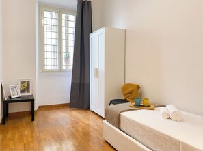 A bedroom with a bed, a wardrobe, a small table with a picture frame, and a window with curtains. - Comfortable apartment located between Villa Borghese, Trinità dei Monti, and the Trevi Fountain (Roma)