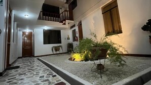 Ένας ευρύχωρος εσωτερικός προαύλιος χώρος με πλακόστρωτο δάπεδο, μια μικρή κηπουρική περιοχή με φυτά και μια σκάλα που οδηγεί σε ανώτερο επίπεδο.