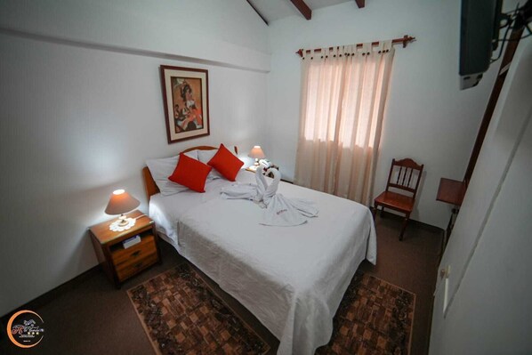 A neatly arranged bedroom with a bed, pillows, a nightstand, a chair, and a painting on the wall. - EL CUMBE INN  (Cajamarca)