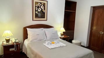 A neatly arranged hotel room with a large bed, a bedside table with a lamp, a telephone, and a framed artwork on the wall.