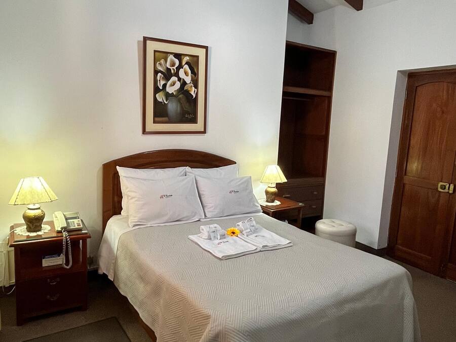 A neatly arranged hotel room with a large bed, a bedside table with a lamp, a telephone, and a framed artwork on the wall.