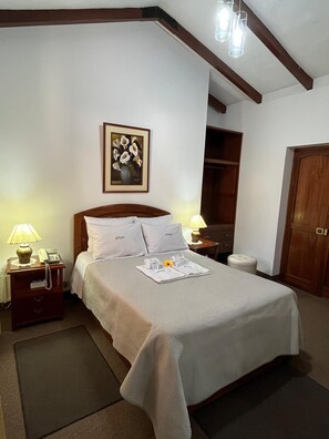 A neatly arranged hotel room with a large bed, a bedside table with a lamp, a telephone, and a framed artwork on the wall. - EL CUMBE INN  (Cajamarca)