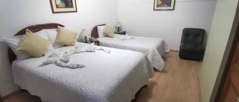 A hotel room with two beds, each with a white bedspread and beige pillows. There are two bedside tables with lamps, and a black chair in the corner.