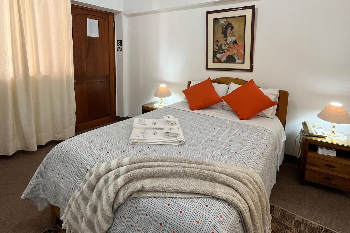A bedroom with a bed, two nightstands, a painting, and a door.