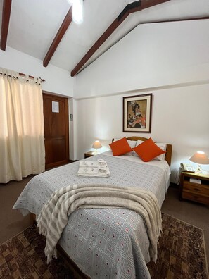 Un dormitorio con cama, dos mesitas de noche, un cuadro y una puerta.