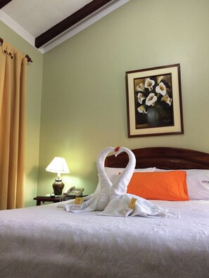 A hotel room with a bed, a framed floral painting, a lamp, and a swan-shaped towel arrangement. - EL CUMBE INN  (Cajamarca)