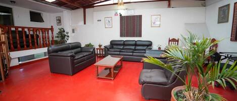 A spacious living room with red flooring, black leather sofas, a wooden coffee table, and a staircase with wooden railings.
