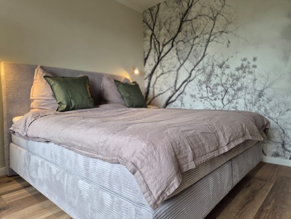 Ein Bett mit grauem Kopfteil, zwei grünen Kissen und einer grauen Bettdecke.
