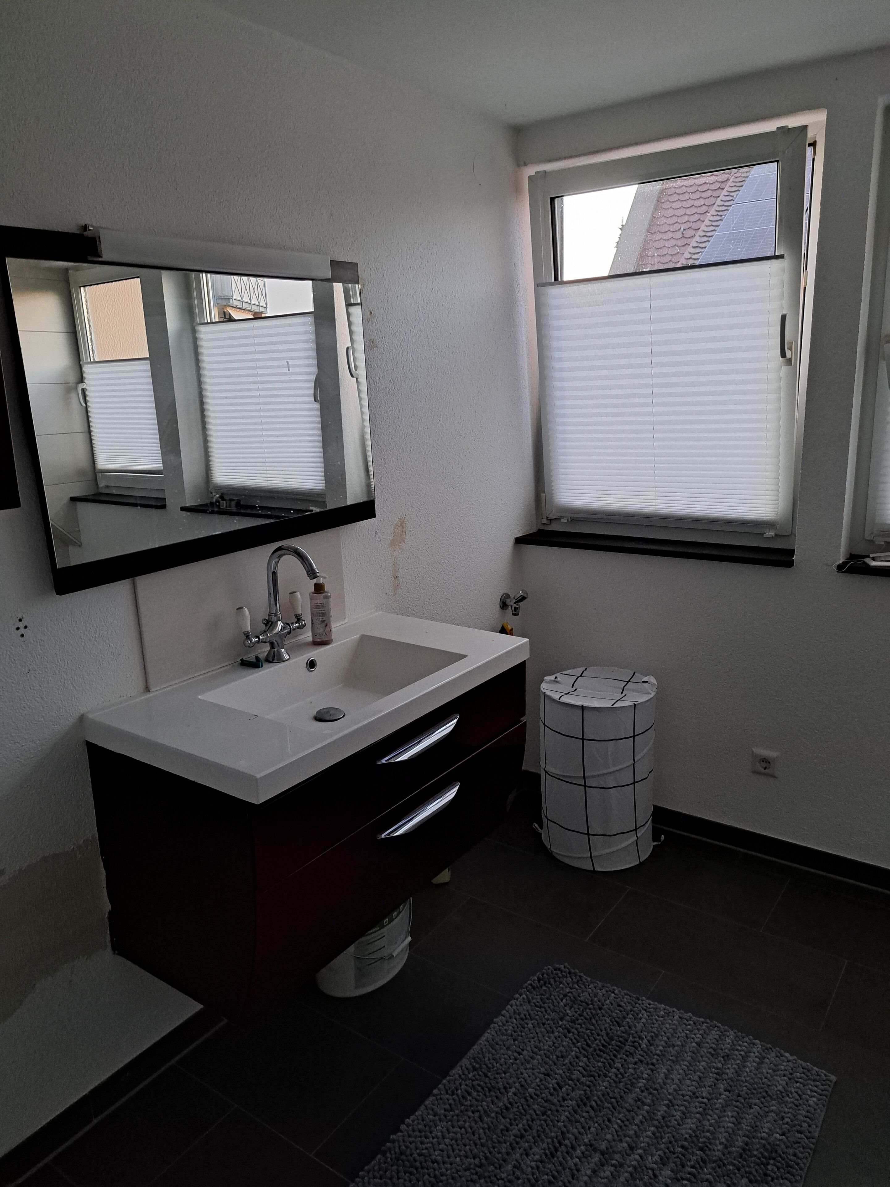 A bathroom with a white sink, dark vanity, mirror, and a window with blinds.
