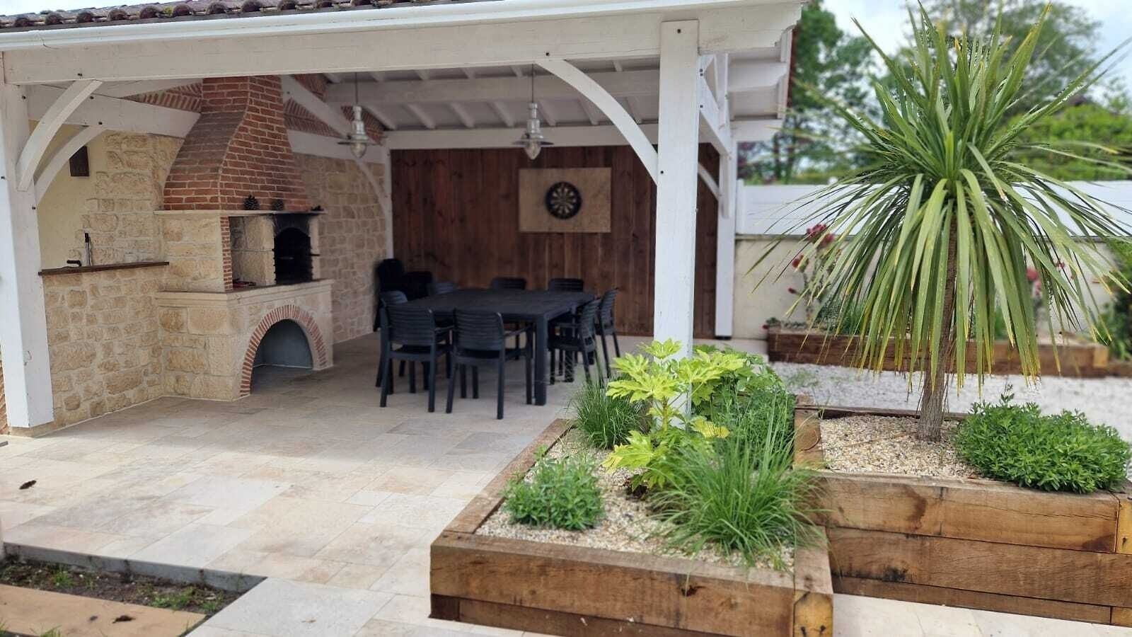 Eine Außenpatio mit Kamin aus Ziegelsteinen, einem Esstisch mit Stühlen und einem Garten mit verschiedenen Pflanzen.