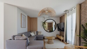 Una sala de estar moderna con un sofá seccional, una mesa de centro redonda, un televisor y un gran ventanal con cortinas.