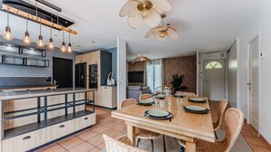 Una cocina moderna con una isla central, iluminación colgante y un comedor con sillas de mimbre y una mesa de madera.