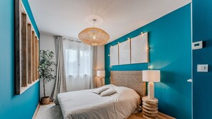 Un dormitorio con una cama, una lámpara colgante, una obra de arte en la pared y una mesita de noche con lámpara.