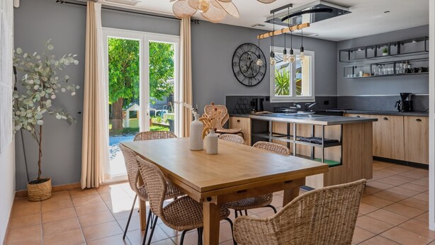 Una cocina moderna con comedor, que incluye una mesa de madera, sillas de mimbre e iluminación colgante.