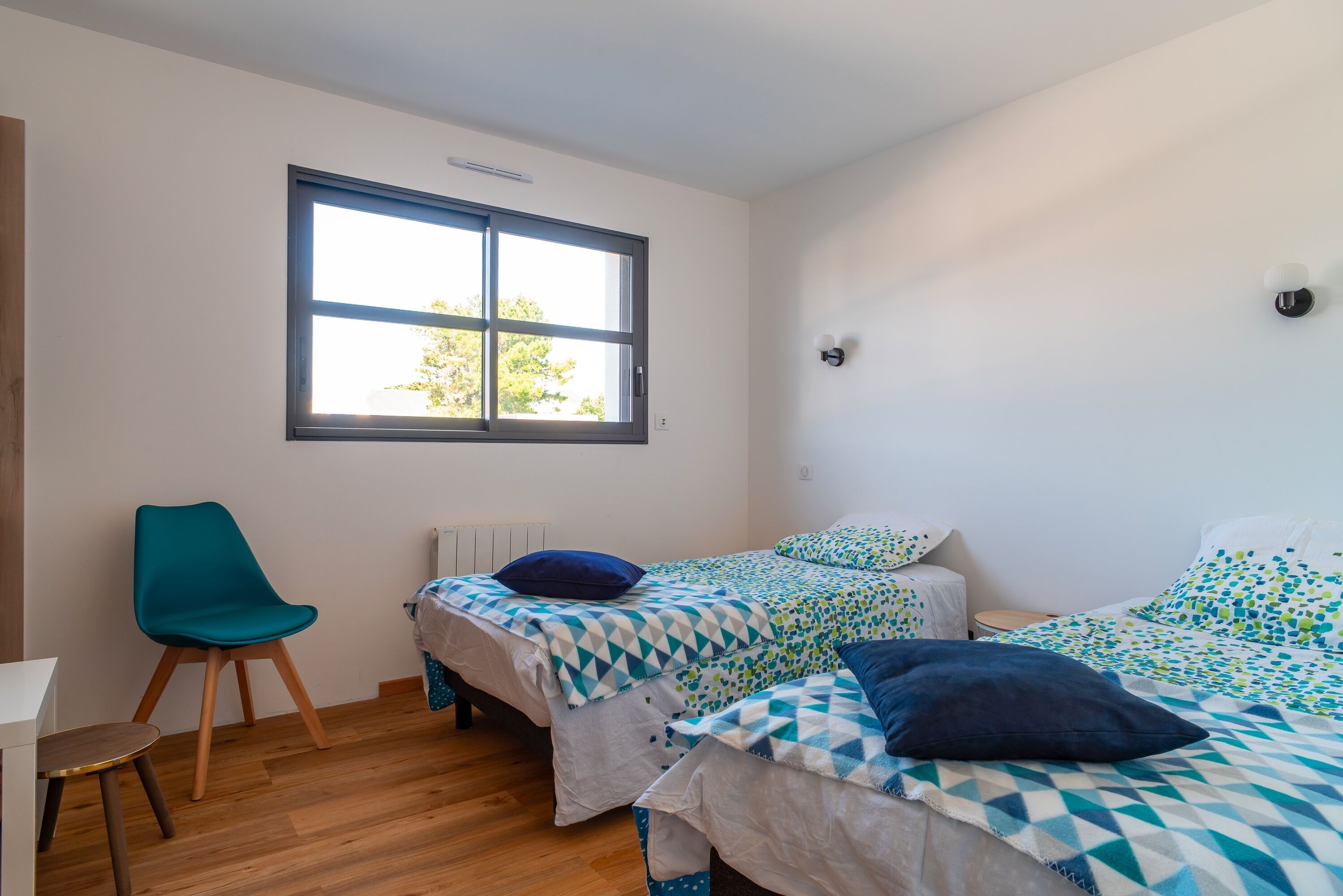 Un dormitorio con dos camas, una silla, un ventanal y un radiador.