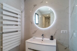 Ein Badezimmer mit weißem Waschtisch, rundem Spiegel und Handtuchhalter.